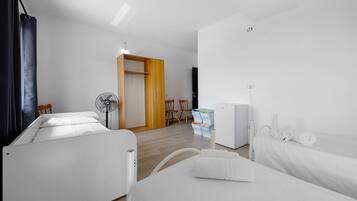 Een hotelkamer met twee bedden, een ventilator, een kledingkast, een klein tafeltje met een stoel en een witte radiator.