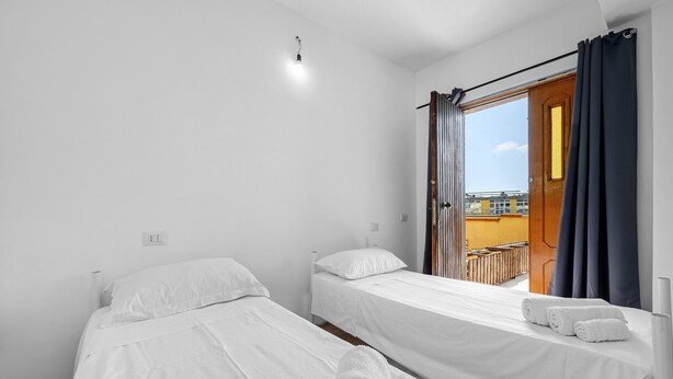A room with two single beds, a window with curtains, and a view of the outside. - Daluef Alloggi – Room 4 (Assemini)