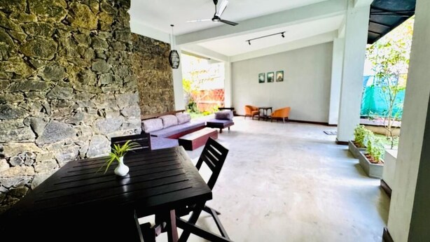 Una habitación con pared de piedra, una mesa negra con una planta, un sofá y un ventilador de techo.