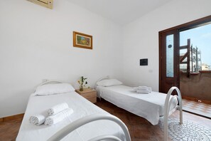 Een hotelkamer met twee eenpersoonsbedden, een tafeltje met een vaas, een schilderij aan de muur en uitzicht door een glazen deur.