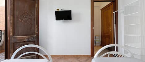 A room with a wooden door, a flat-screen TV mounted on the wall, and two white chairs with a table.
