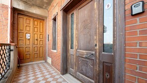 A building entrance with a checkered floor, a wooden door with a number plate, and a metal gate. - Daluef Alloggi - Room 9 (Assemini)