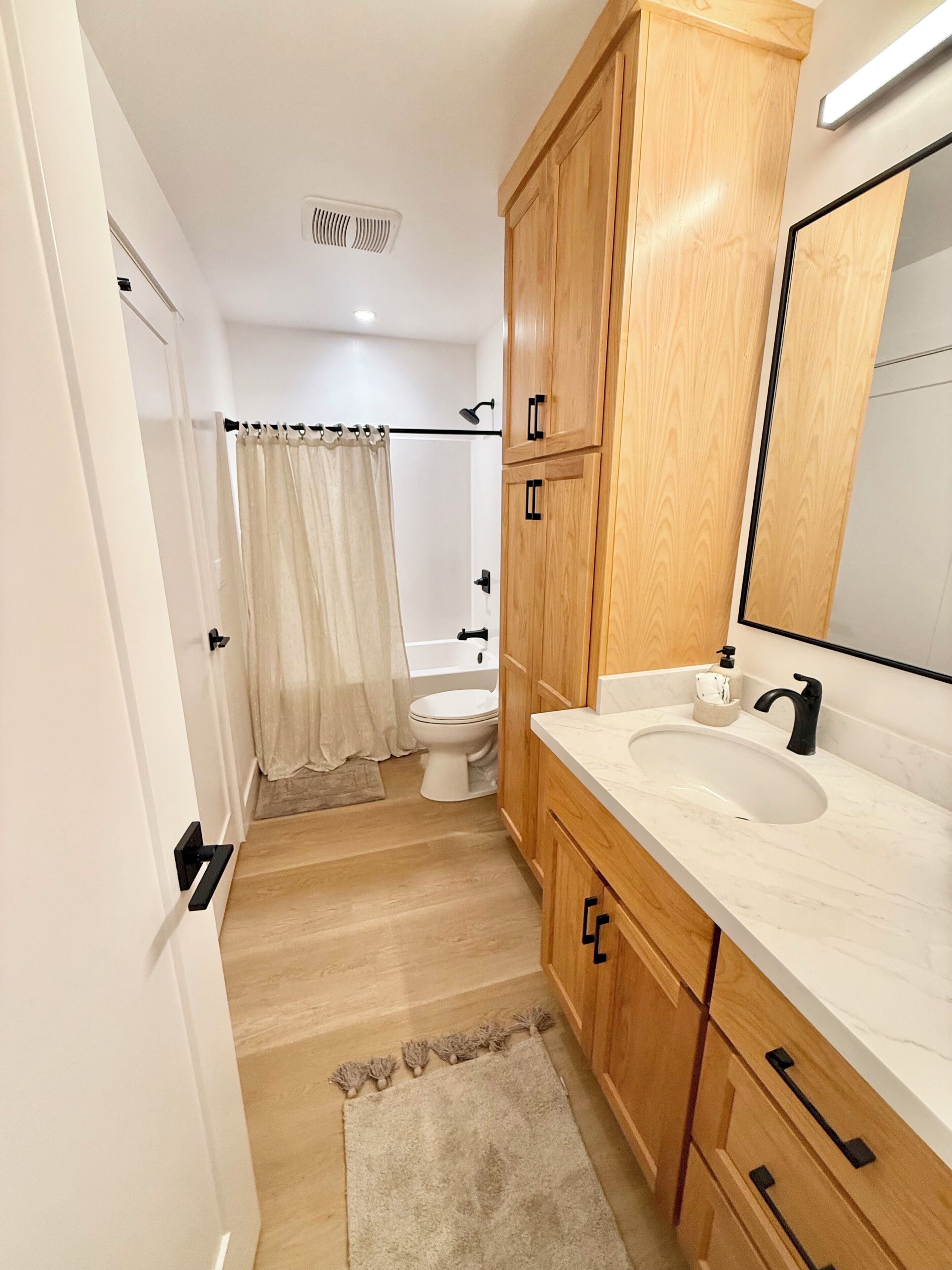 A bathroom with a toilet, sink, wooden cabinets, a mirror, and a shower curtain.