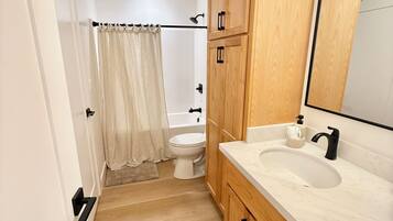A bathroom with a toilet, sink, wooden cabinets, a mirror, and a shower curtain.