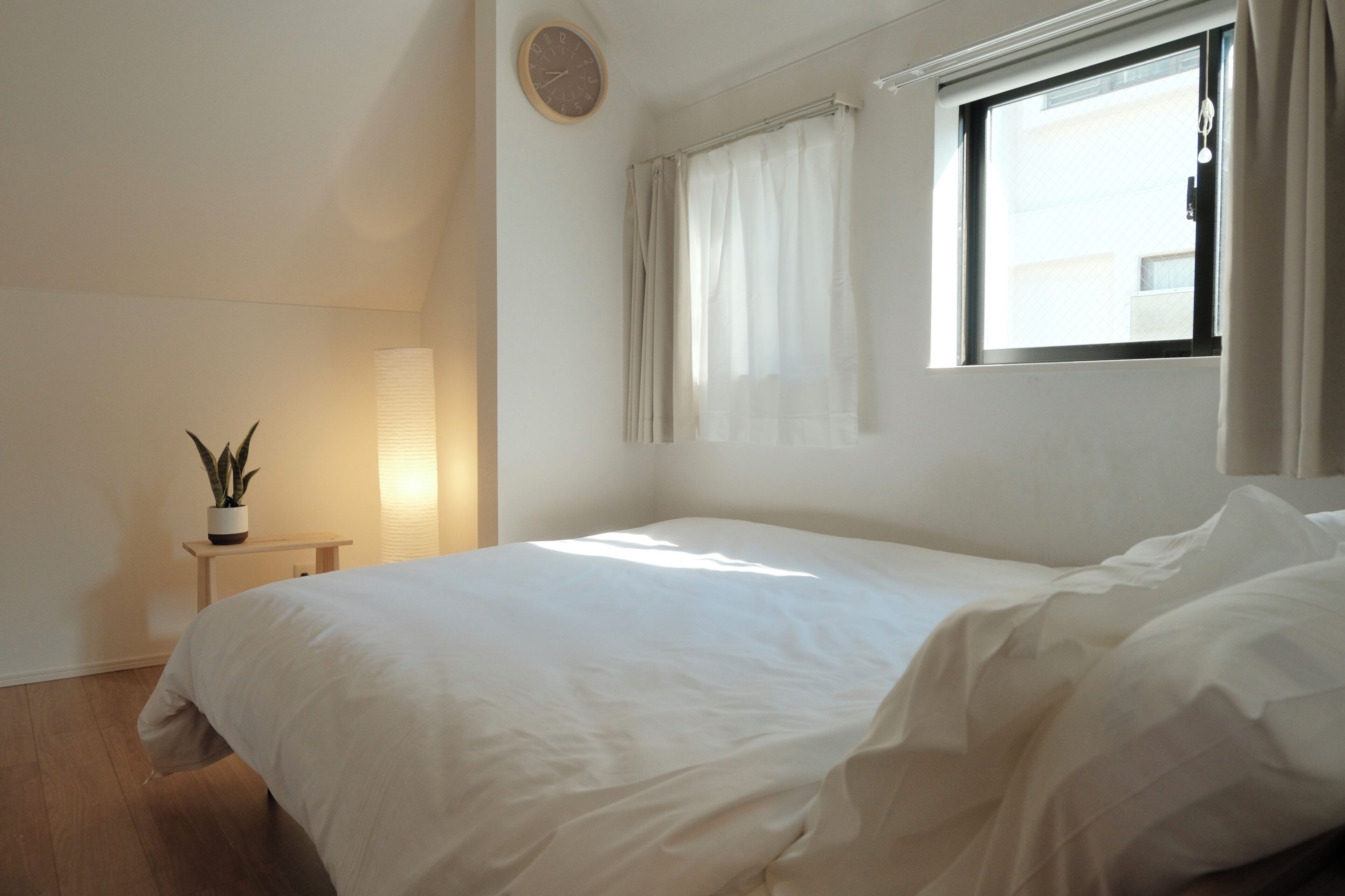 Une chambre à coucher avec un lit, une table de chevet avec une lampe, une plante en pot et une fenêtre avec des rideaux.
