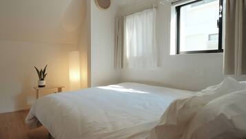 Une chambre à coucher avec un lit, une table de chevet avec une lampe, une plante en pot et une fenêtre avec des rideaux.