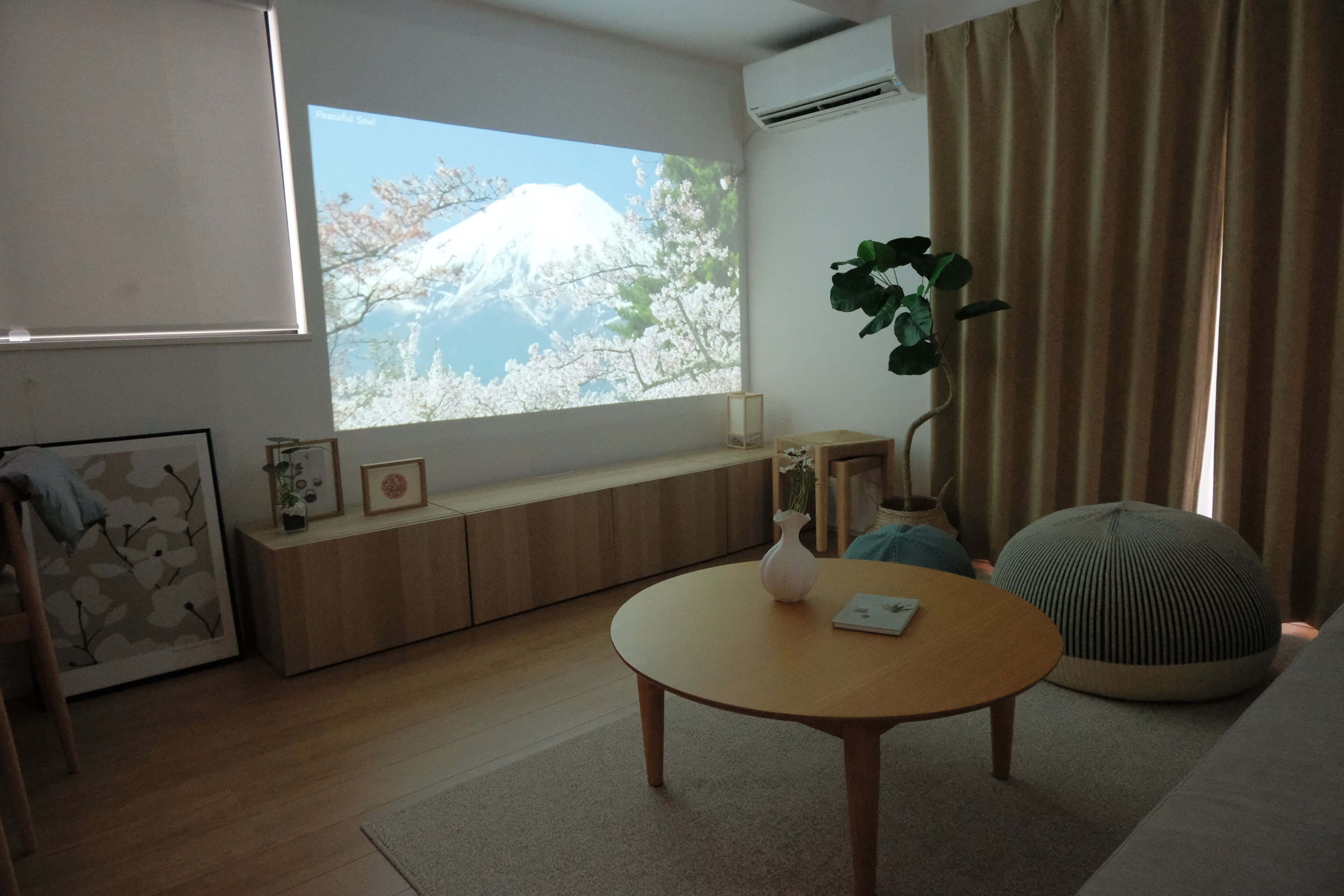 A modern living room with a large window, a round wooden table, a potted plant, and a sofa.