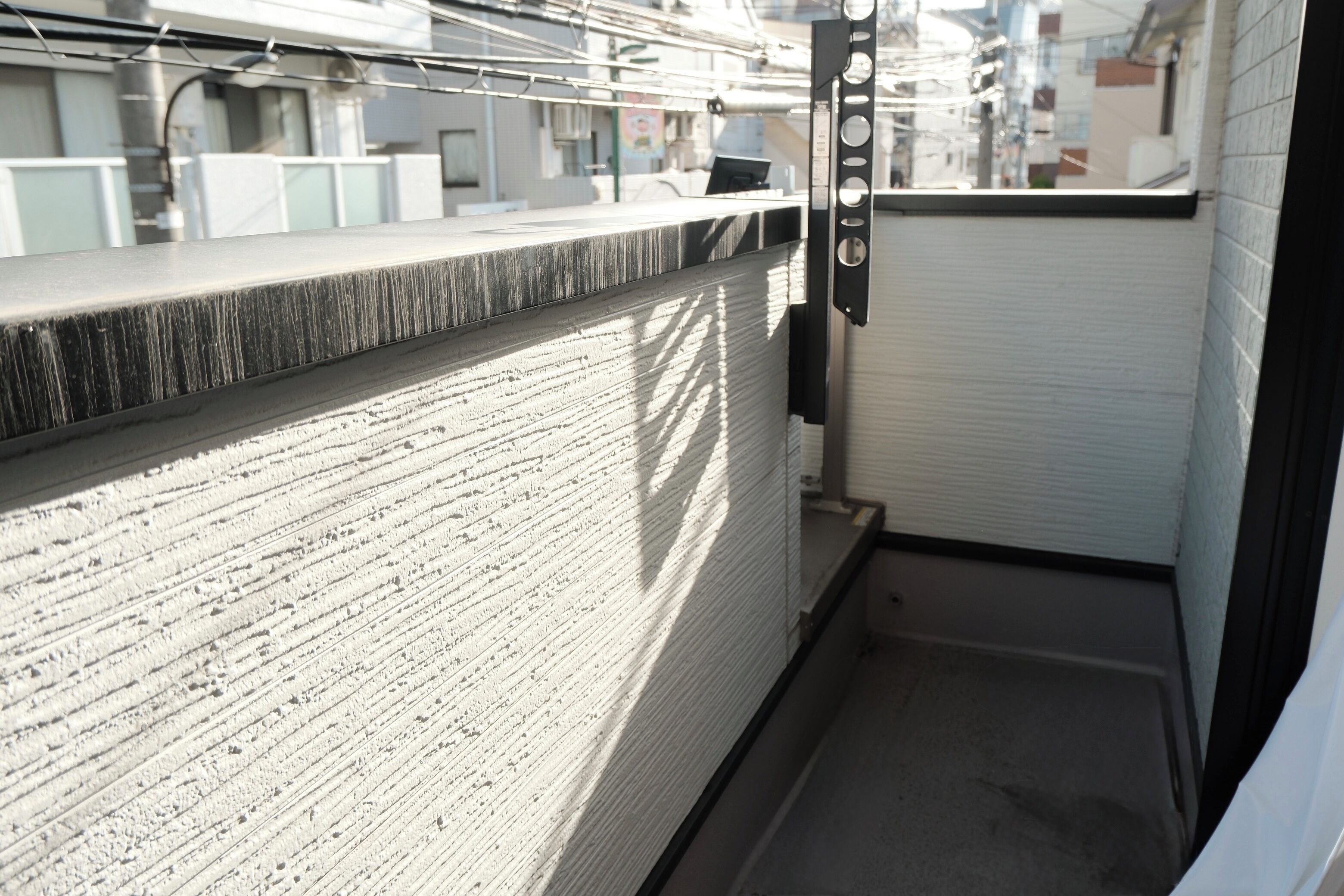 A narrow balcony with a metal railing, a concrete floor, and a view of neighboring buildings.