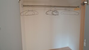 Una stanza con pavimento in legno, parete bianca e un'asta per tende in metallo con tre attaccapanni vuoti.