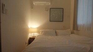 Una camera d'albergo con un letto, un comodino, una lampada, un condizionatore e un quadro appeso al muro.