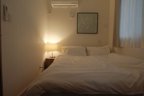 Habitación de hotel con cama, mesita de noche, lámpara, aire acondicionado y un cuadro en la pared.