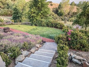 A landscaped garden with a stone pathway leading to a grassy area, surrounded by various shrubs and flowering plants. - Serrano Village Villa (El Dorado Hills)