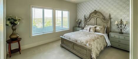 Quarto com uma cama grande, mesa de cabeceira, abajur e um vaso com flores.