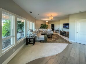 A spacious living room with a large window, a sofa set, a coffee table, and a fireplace. - Serrano Village Villa (El Dorado Hills)