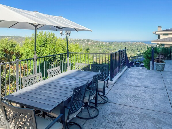 An outdoor patio with a table and chairs, a white umbrella, and a view of the landscape. - Serrano Village Villa (El Dorado Hills)