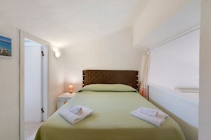 Un lit simple avec une tête de lit matelassée, une lampe de chevet et deux serviettes pliées.