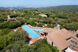 Une grande piscine entourée d’une végétation luxuriante, avec une vue sur la mer et les collines en arrière-plan.