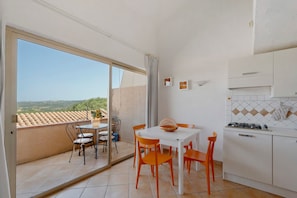 A balcony with a table and chairs, a view of the countryside, and a kitchen with white cabinets and a gas stove. - Apartment 'Flat Pace E Mare' with Sea View, Shared Pool and Air Conditioning (Pulcheddu)