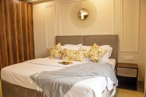 A neatly made bed with floral pillows, a throw blanket, and a wall-mounted light fixture.