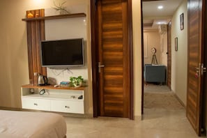 Une chambre d’hôtel avec une télévision posée sur une étagère en bois, un lit, un bureau avec une bouilloire et une porte donnant sur une autre pièce.