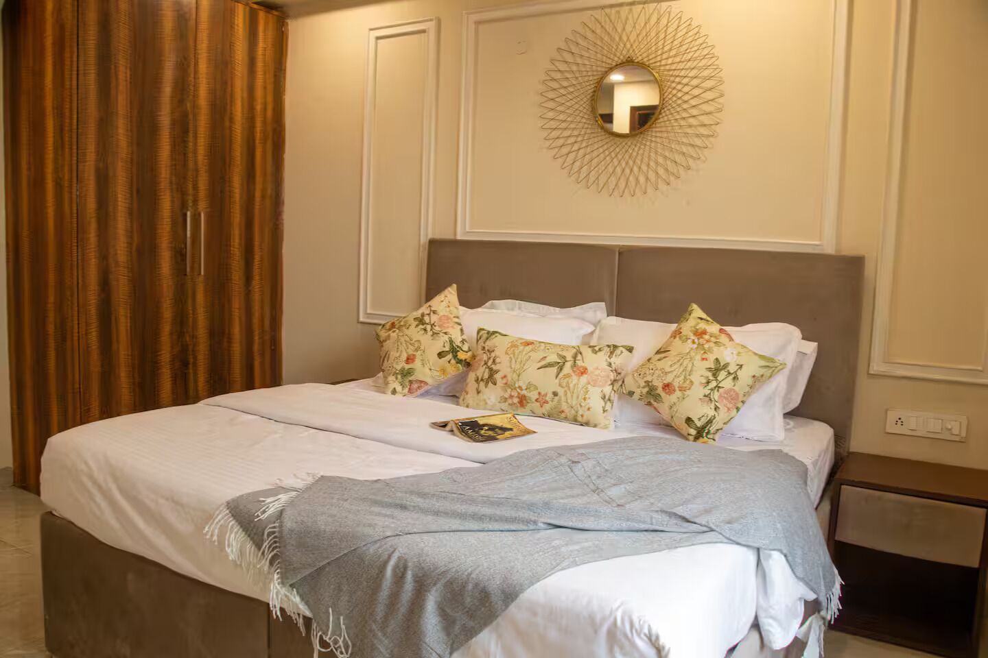 A neatly made bed with floral pillows, a throw blanket, and a wall-mounted light fixture.