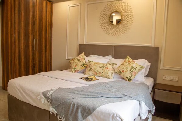 A neatly made bed with floral pillows, a throw blanket, and a wall-mounted light fixture.