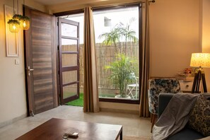 Une pièce dotée d’une porte-fenêtre coulissante donnant sur un balcon, d’un canapé, d’une petite table et d’une lampe.