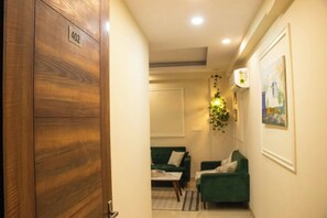 A hallway with a wooden door marked '402', leading to a room with two green sofas and a small table. - 402 - Designer 1BR Retreat - Golf Course Rd (Gurugram)