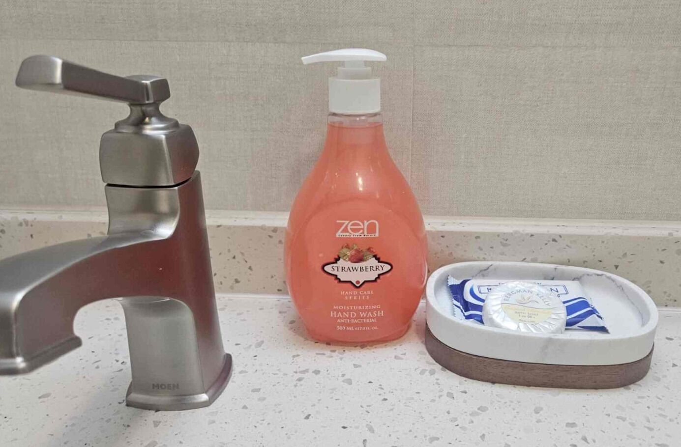 A bathroom sink with a modern faucet, a bottle of hand soap, and a soap dish with a bar of soap.