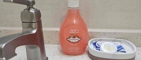 A bathroom sink with a modern faucet, a bottle of hand soap, and a soap dish with a bar of soap.
