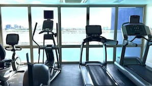 Un gimnasio con cintas de correr, elíptica y bicicleta estática, con vista a un cuerpo de agua a través de amplias ventanas.