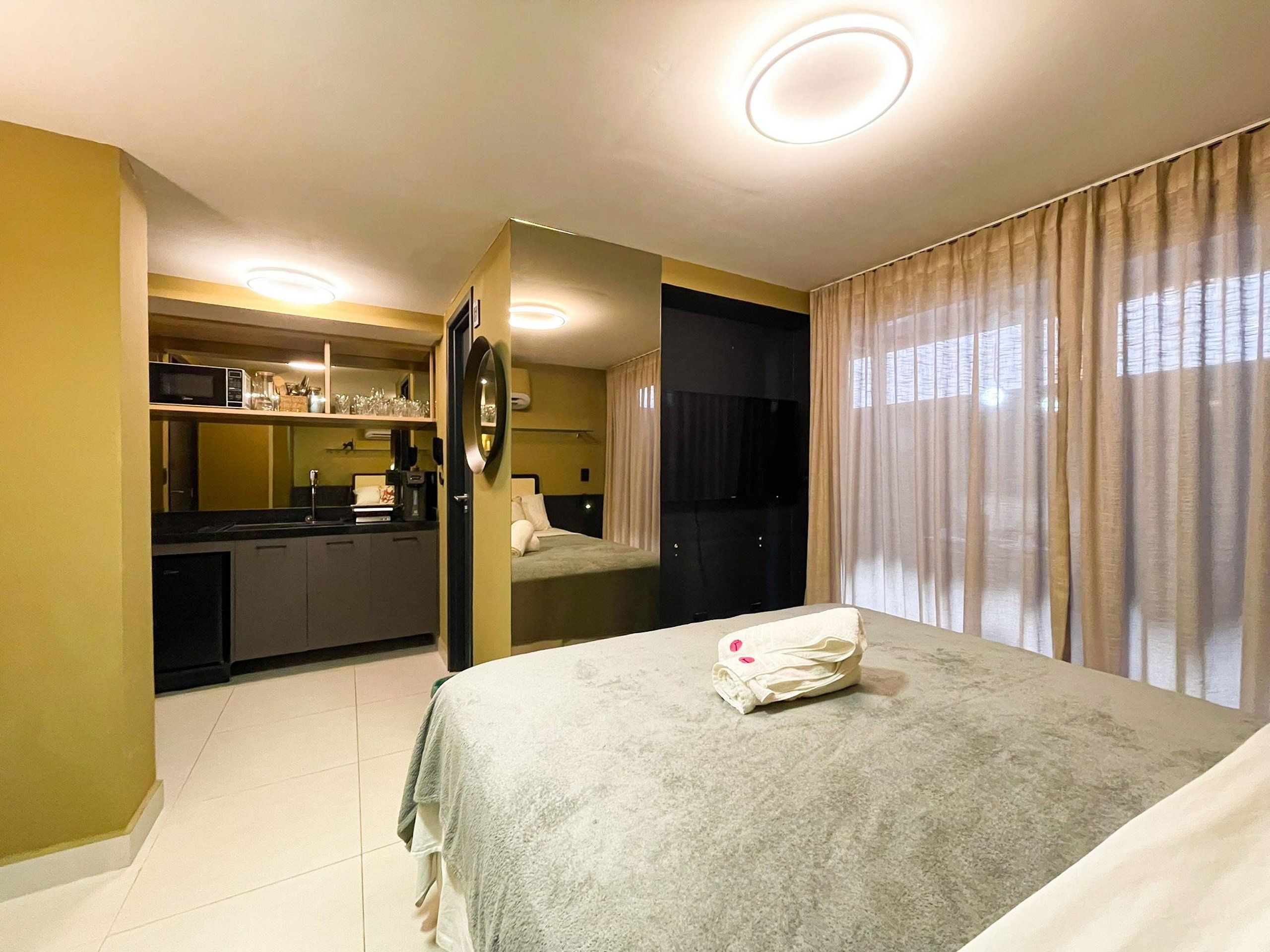 A hotel room with a bed, a small kitchenette, a mirror, and a bathroom.