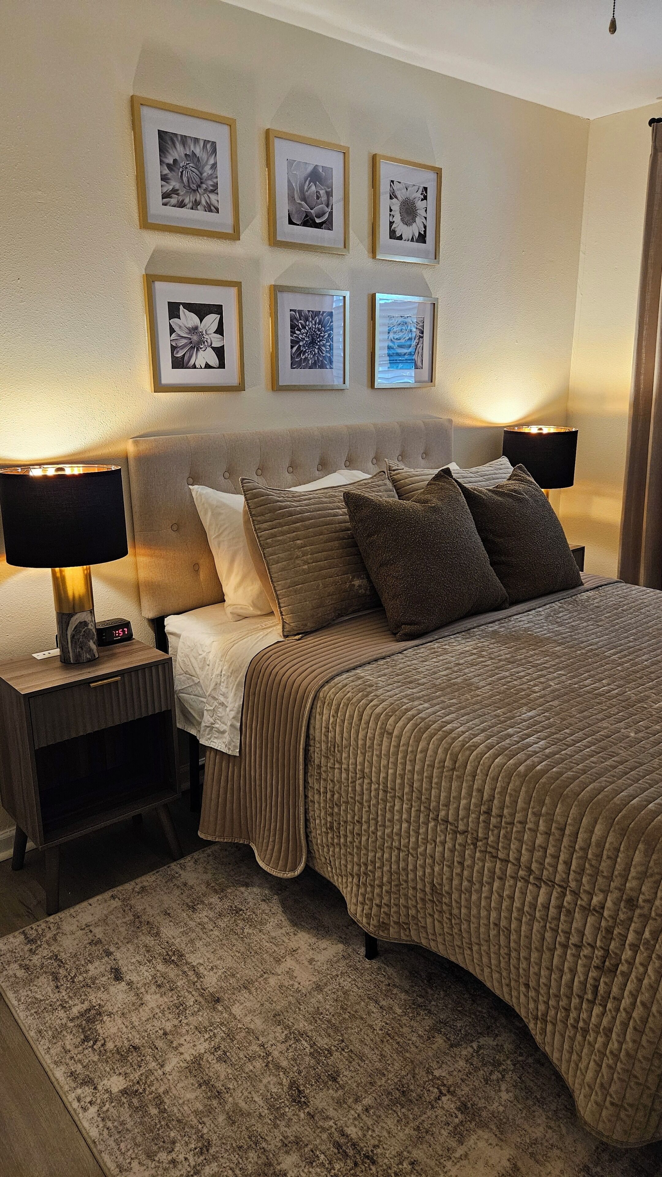 A bedroom with a bed, nightstands, a clock, and framed floral artwork on the wall.