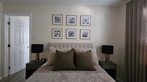 Ein Schlafzimmer mit einem Bett, zwei Nachttischen, einer Tür und sechs gerahmten Bildern an der Wand.