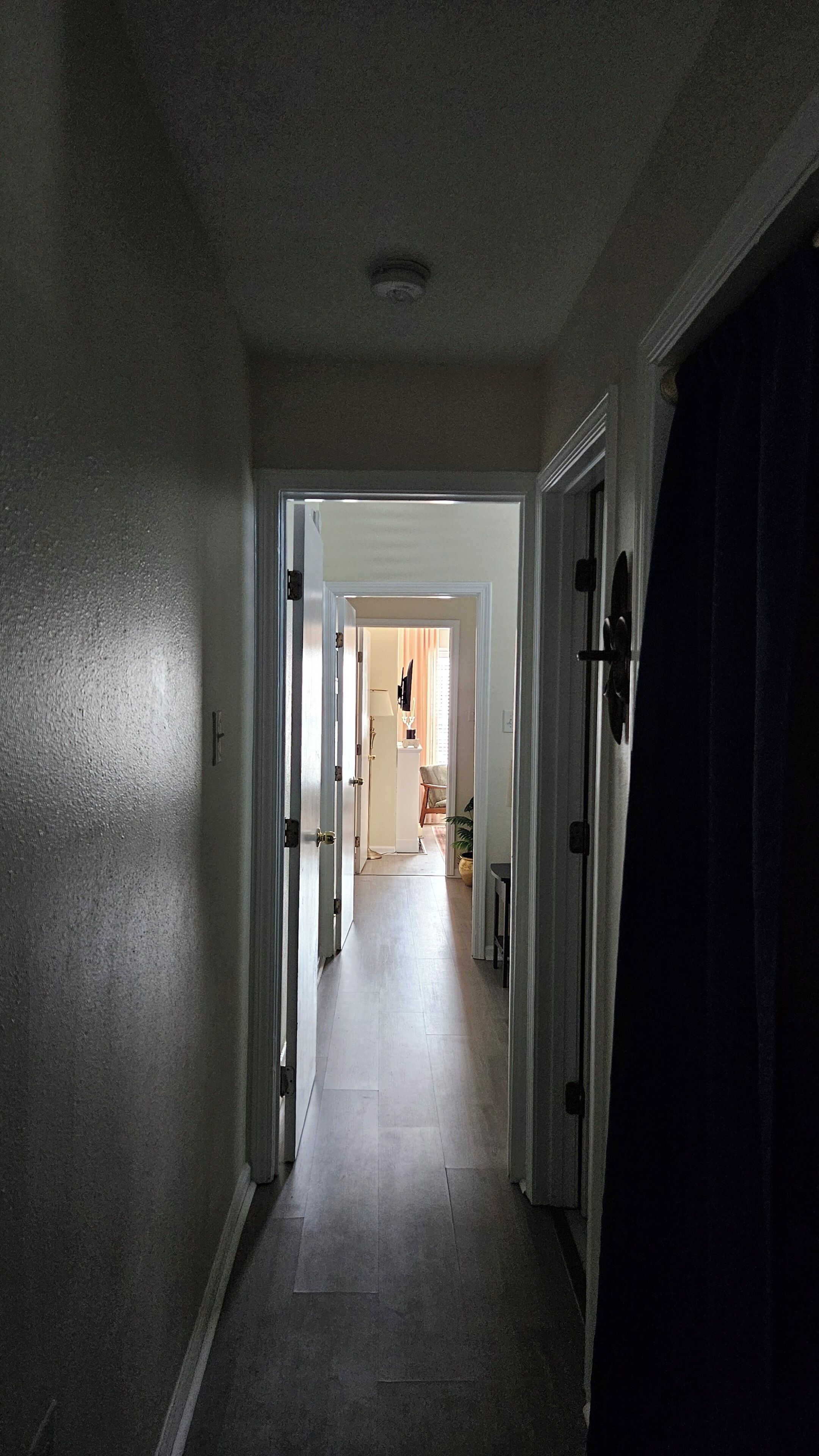 Un pasillo con una puerta a la derecha que da a una habitación con una silla y una lámpara.