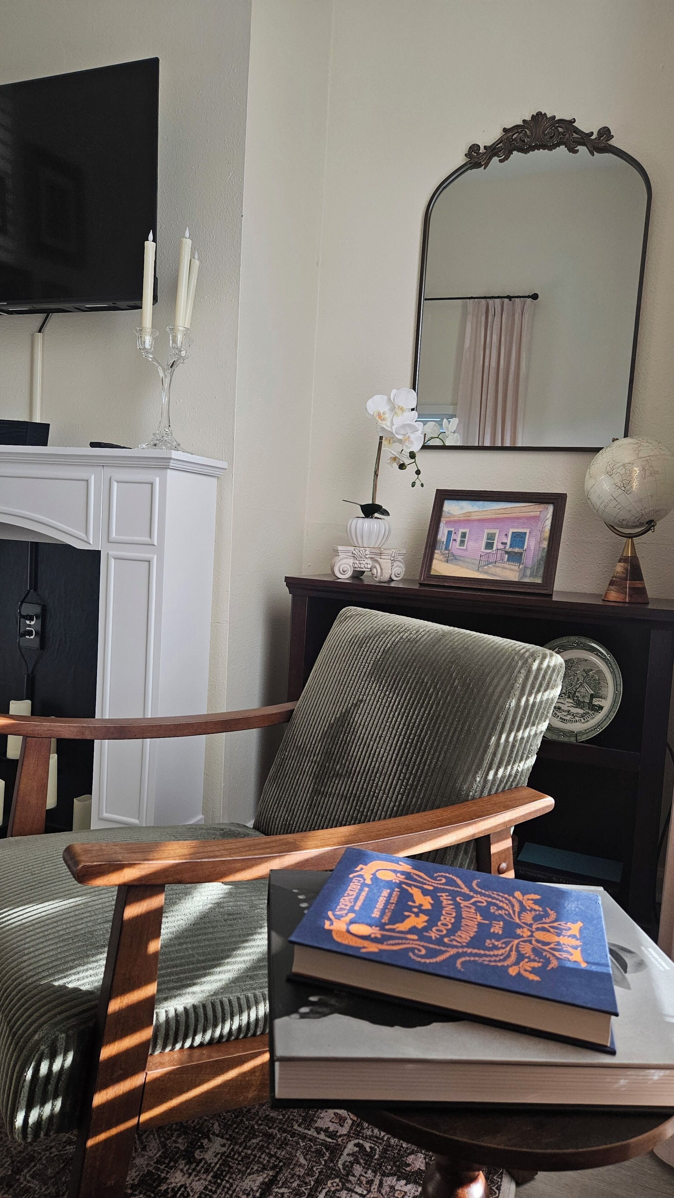 A room with a wooden chair, a table with books, a globe, and a mirror on the wall.