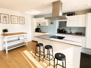 A modern kitchen with white cabinetry, a central island with stools, and a microwave above the island. - Bright and Spacious 2BDR Flat Westfield Stratford (Greater London)