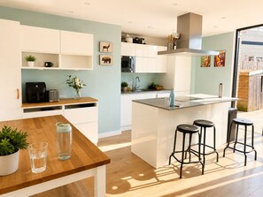 Una cocina moderna con armarios blancos, una isla central con taburetes, una cafetera y un microondas.
