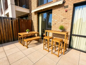 Un patio al aire libre con una mesa y bancos de madera, una planta en maceta y un muro de ladrillo.