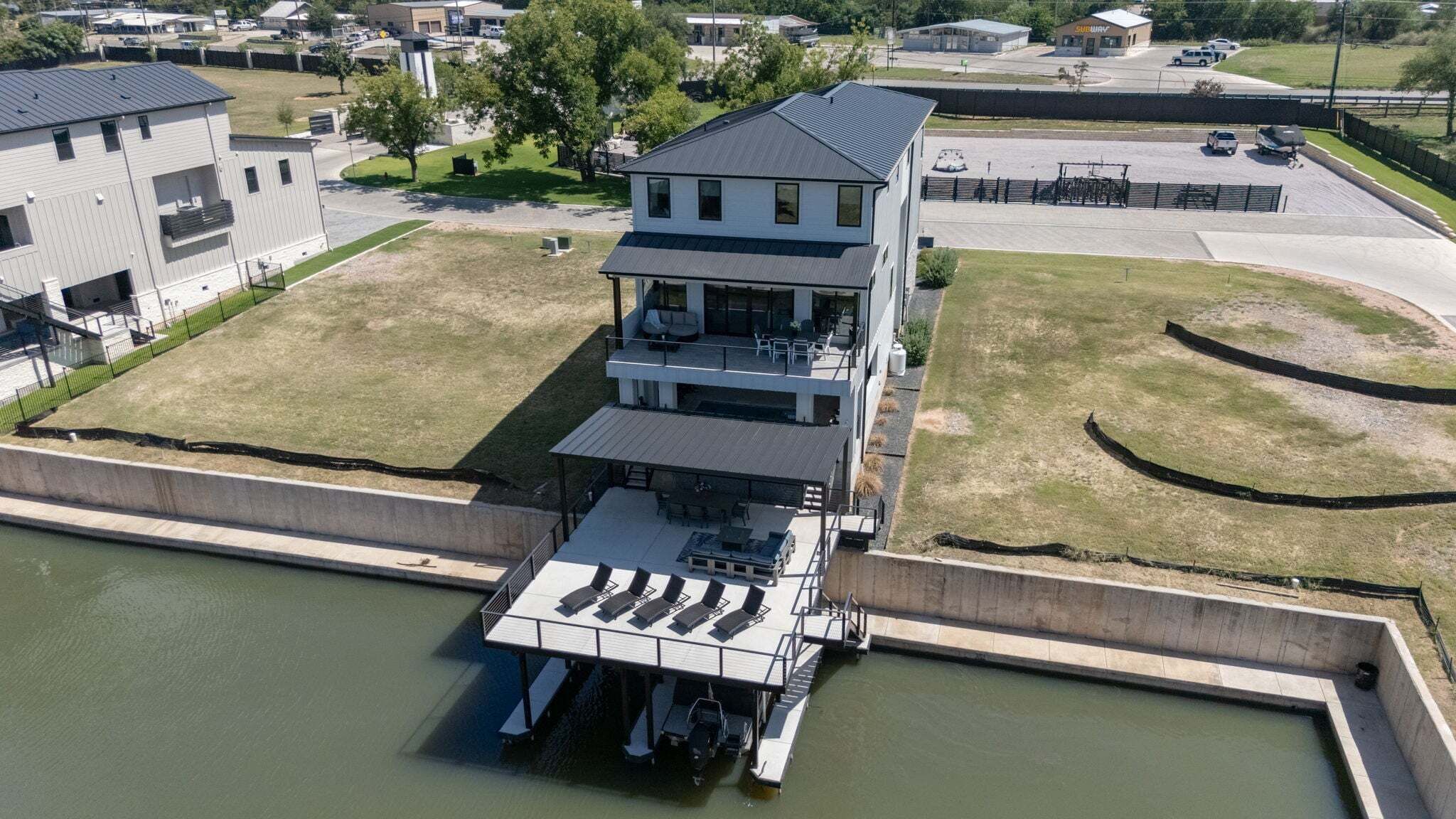 A modern two-story building with a flat roof, a covered outdoor deck with seating, and a dock extending into a body of water.