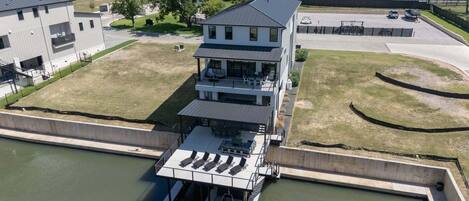 Ein modernes, zweistöckiges Gebäude mit flachem Dach, einer überdachten Terrasse mit Sitzgelegenheiten und einem Steg, der sich ins Wasser erstreckt.