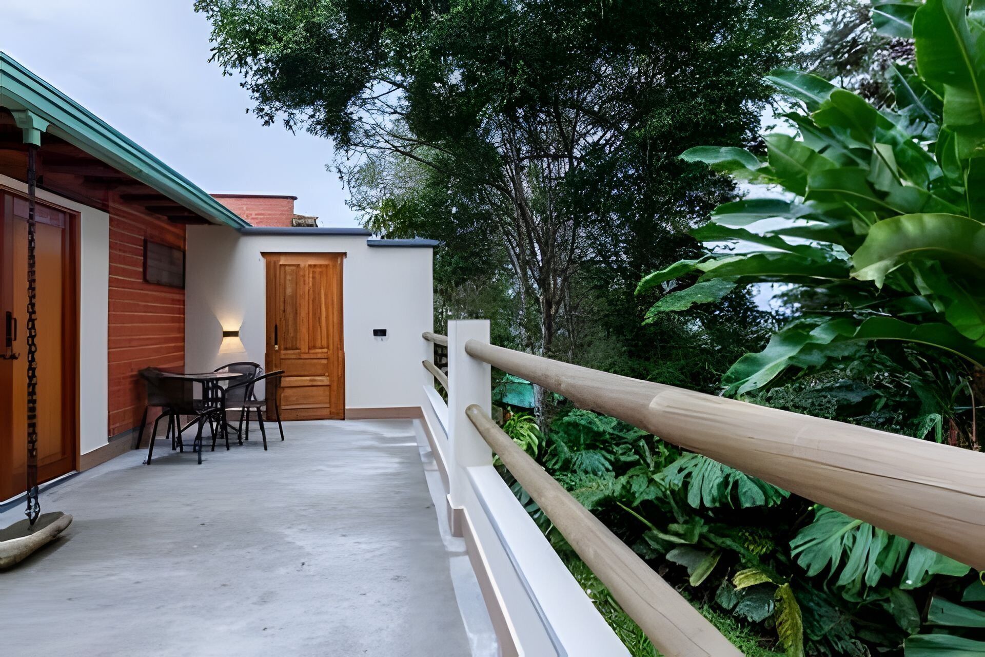 A covered outdoor area with a wooden door, a table with chairs, and a concrete floor.