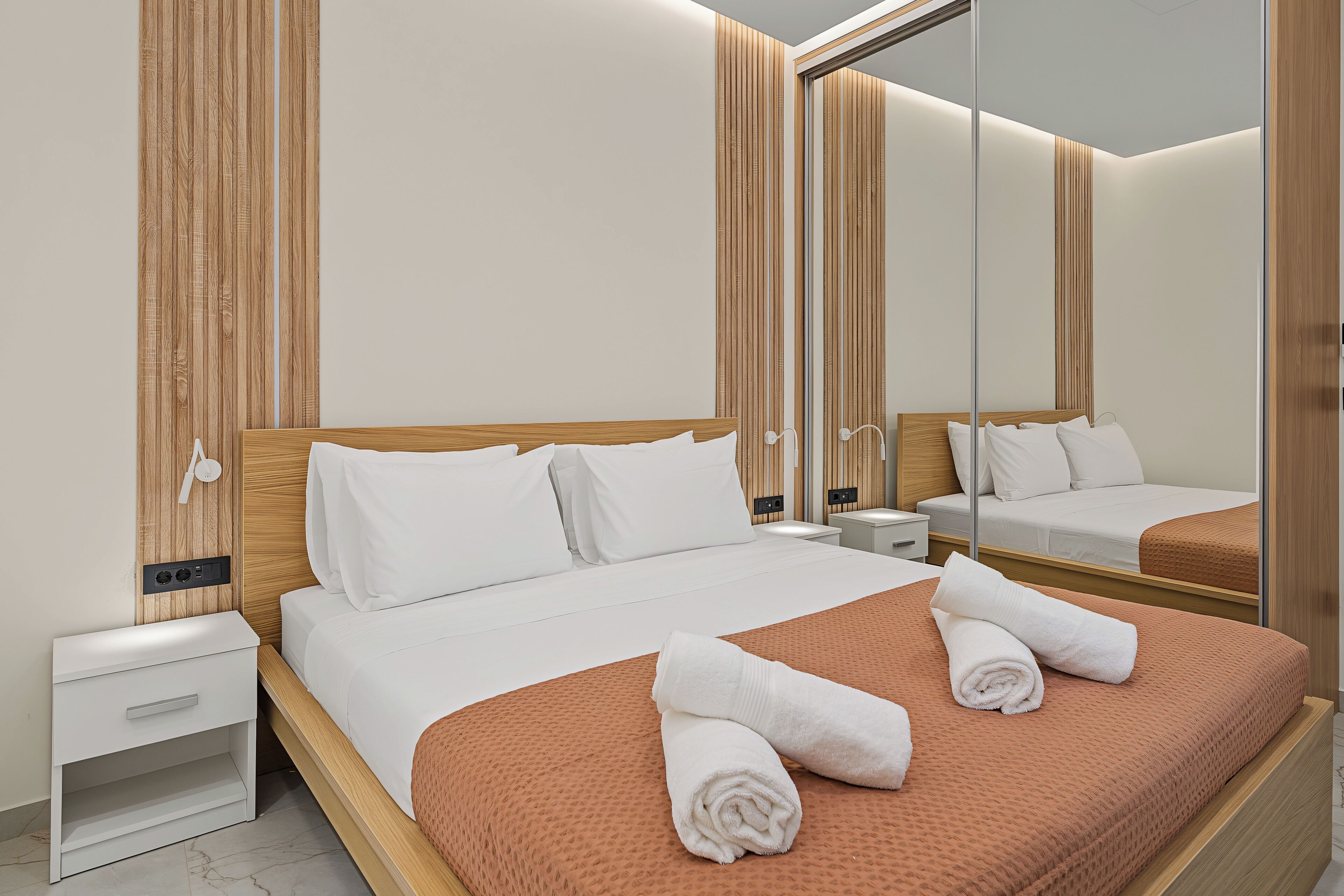 Une chambre d’hôtel avec un grand lit, une table de chevet, un miroir et un mur recouvert de panneaux en bois.