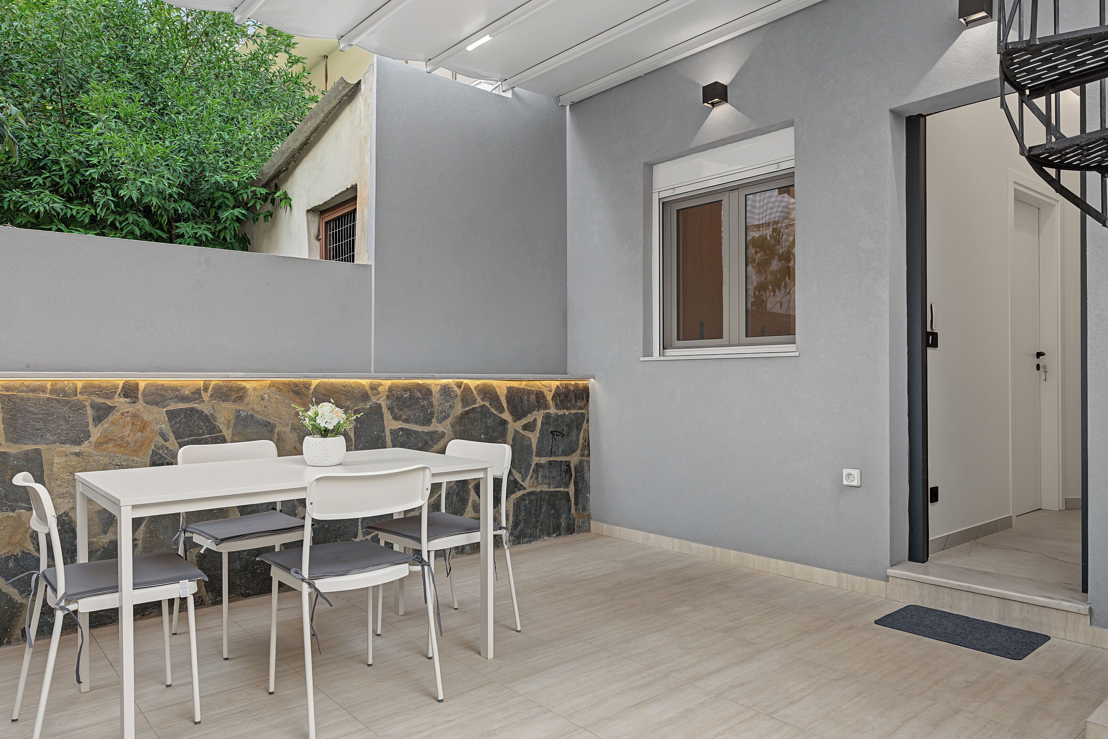 Un espace de restauration extérieur moderne, avec un mur en pierre, une table blanche et des chaises.