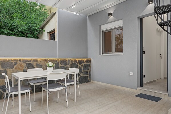 A modern outdoor dining area with a stone wall, a white table, and chairs.