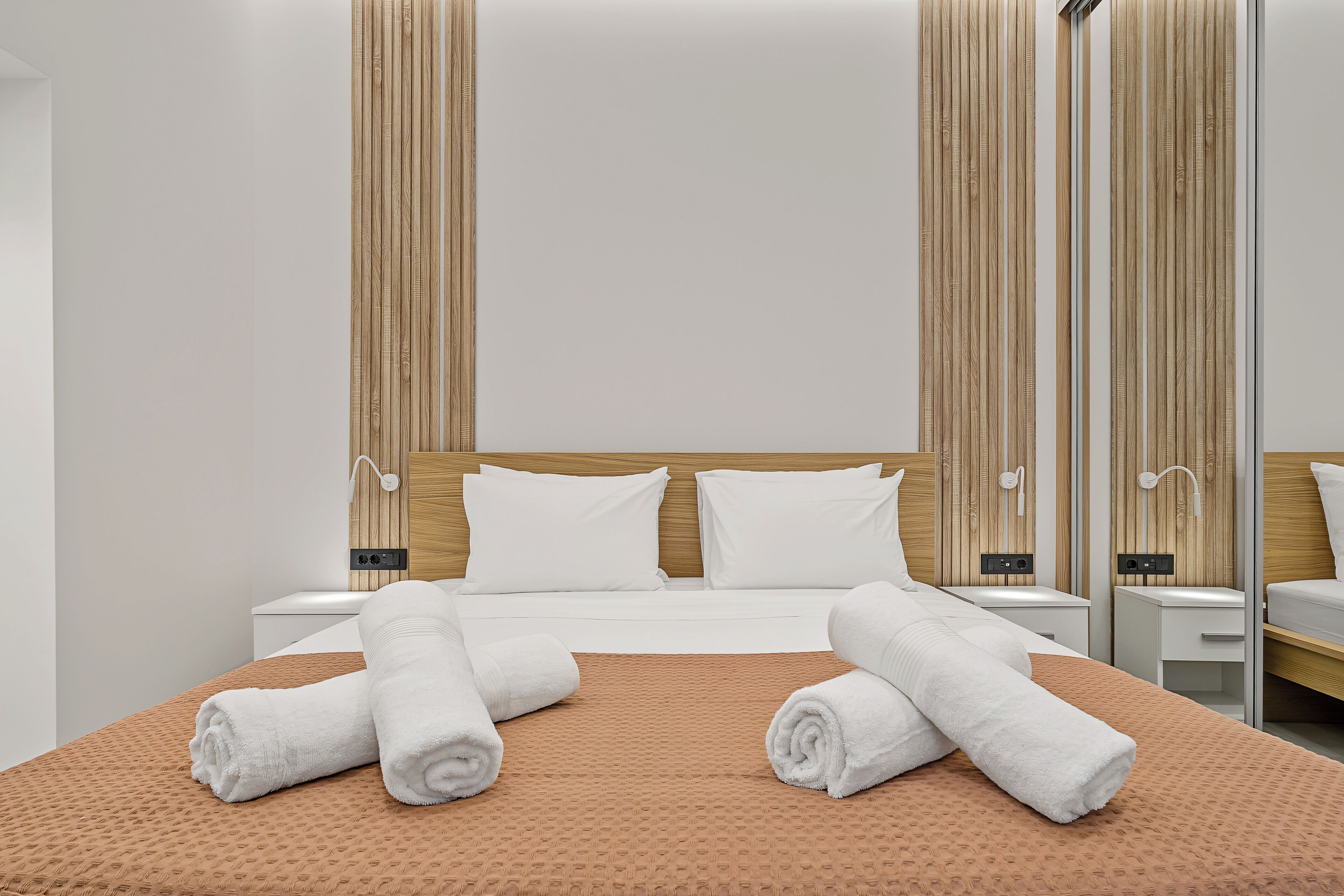 Une chambre d’hôtel avec un grand lit, deux tables de chevet, une tête de lit en bois et un miroir.