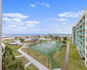 Ein Tennisplatz, umgeben von einem Hotelgebäude mit Blick auf den Strand.