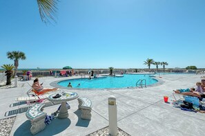 Ein Poolbereich mit Liegestühlen und Tischen, ein Schwimmbecken und Blick auf den Ozean.