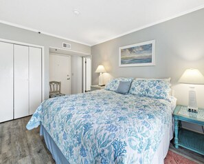 A bedroom with a bed, two bedside lamps, a nightstand, a chair, a door, and a painting on the wall. - Beachfront 2BR, Stunning Gulf Views, Indoor/Outdoor Pools, Hot Tub, Tennis Court (Gulf Shores)
