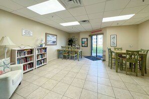 A library with bookshelves, a reading table, and chairs. - Beachfront 2BR, Stunning Gulf Views, Indoor/Outdoor Pools, Hot Tub, Tennis Court (Gulf Shores)